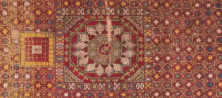 Detalle de una alfombra de seda con un tablero cuadriculado a la izquierda y un medallón octogonal al centro.