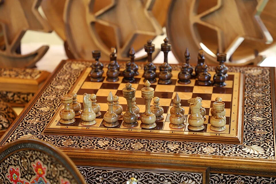Tablero de ajedrez de madera tallada con piezas torneadas, en una feria de artesanía.